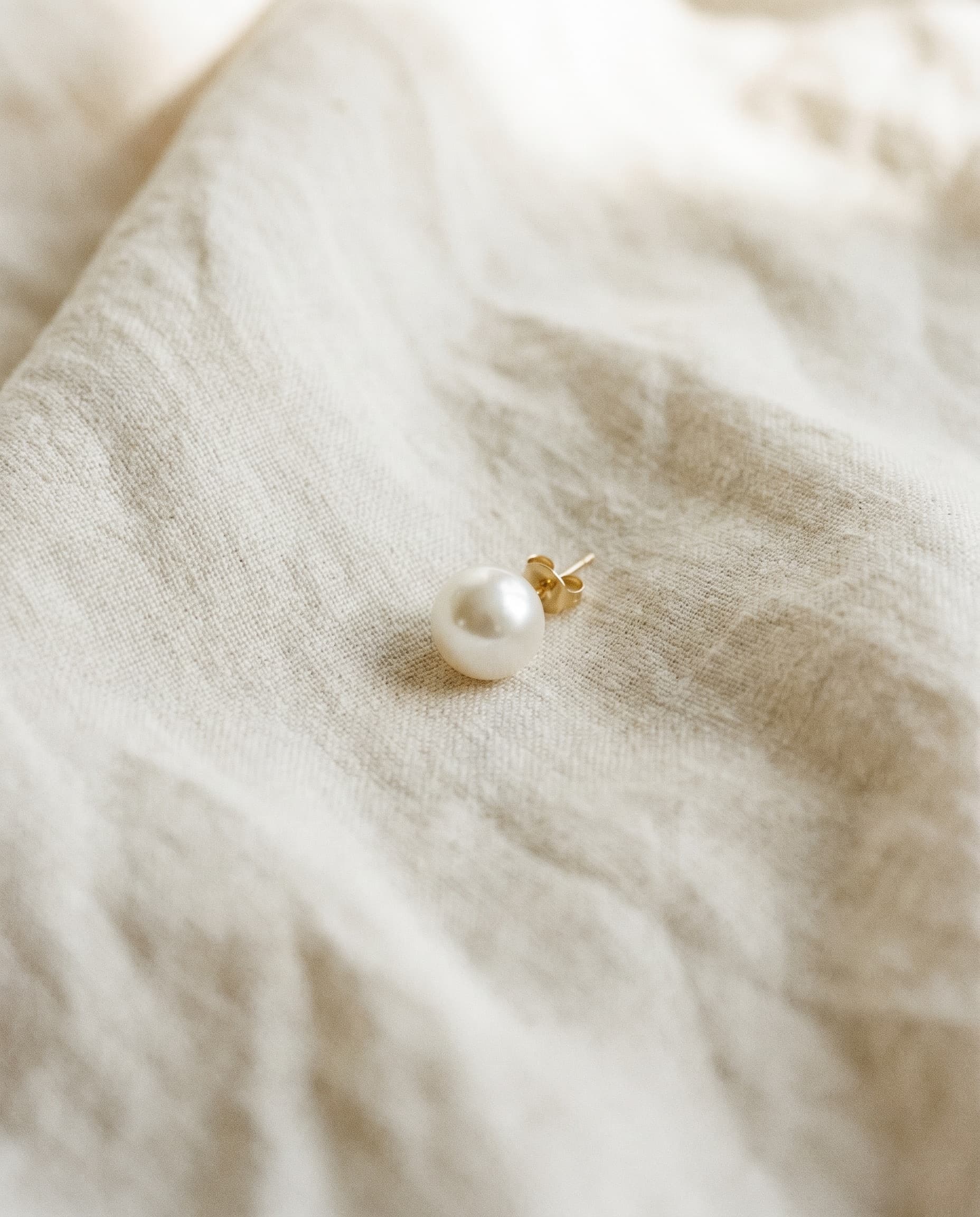 Editorial still life — a single pearl earring on linen